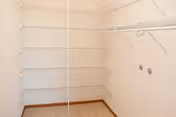 Empty walk-in closet with multiple white wire shelves and hanging rods on beige walls and a tiled floor.