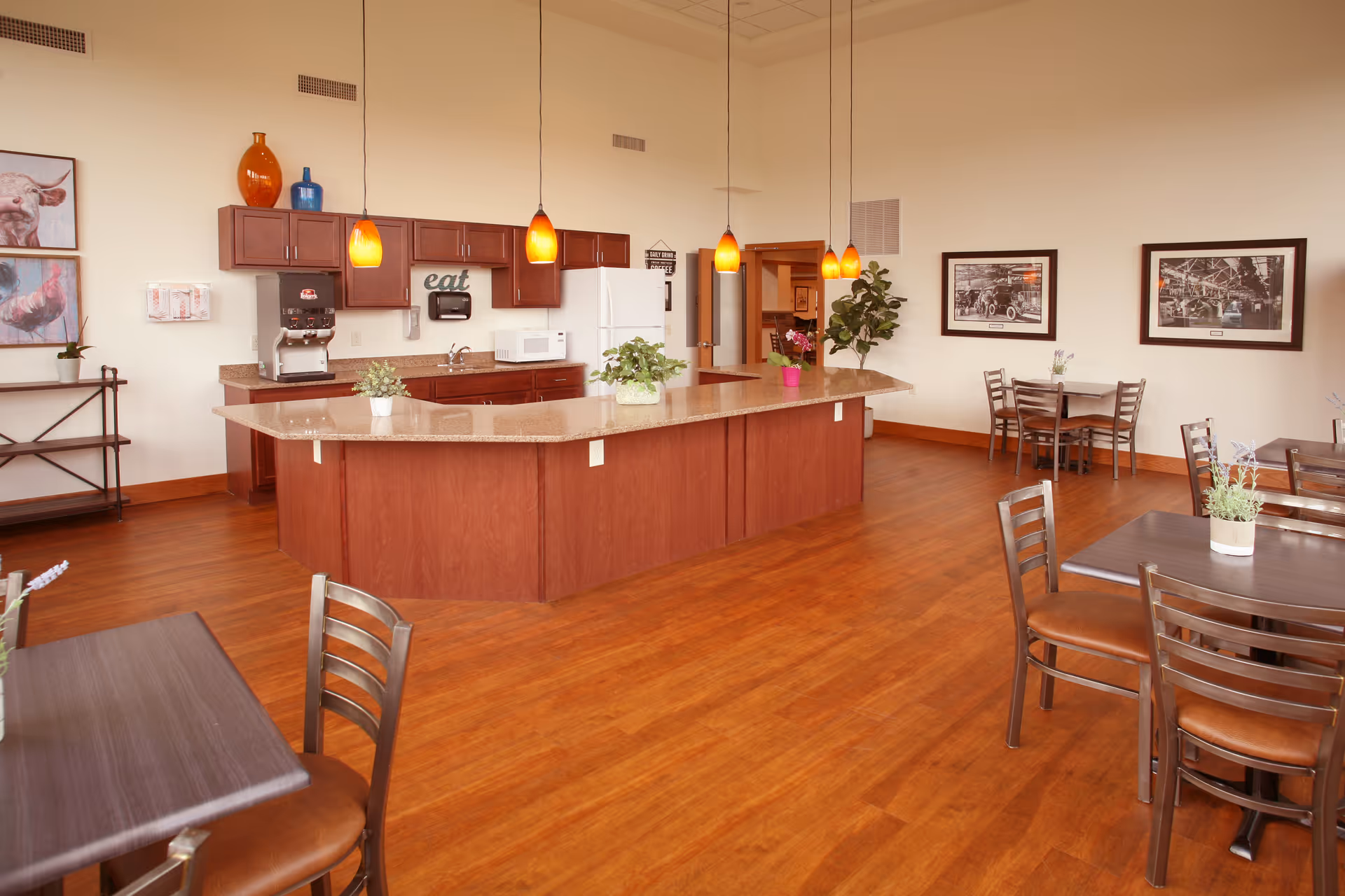 Communal dining area with a large central kitchen island, pendant lights, and several tables and chairs.