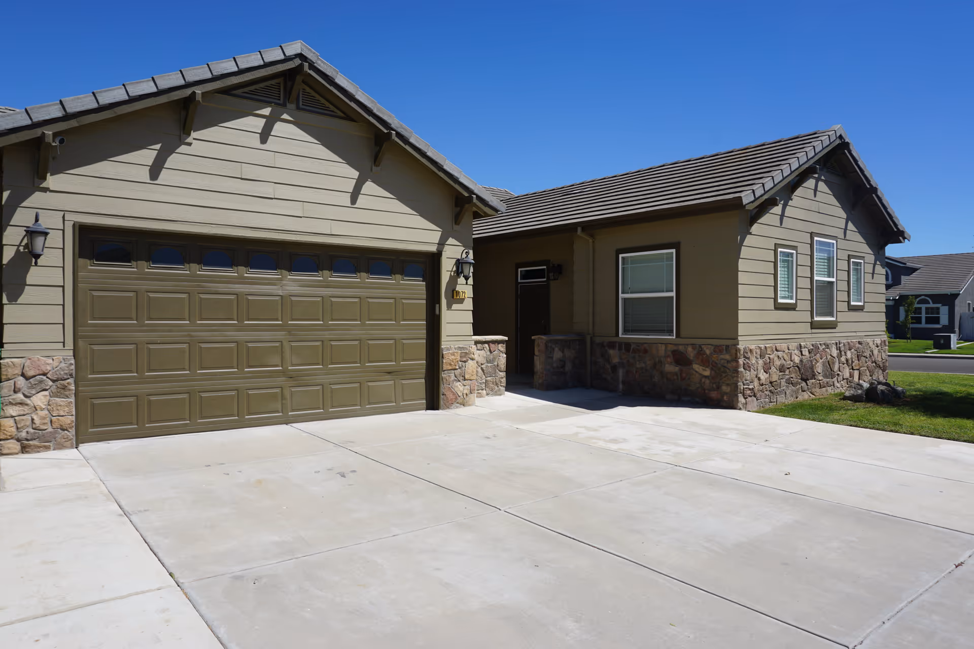 Front exterior of a single-story home featuring a two-car garage, stone siding, and a concrete driveway under a clear blue sky.