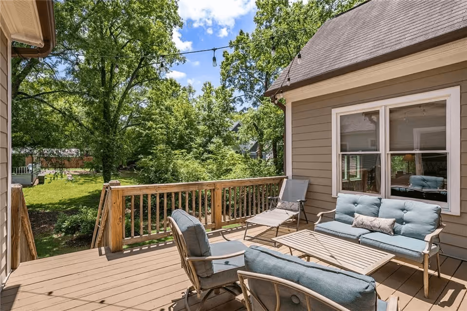 Sunlit wooden deck with cushioned outdoor seating and lounge chairs overlooking a green backyard.