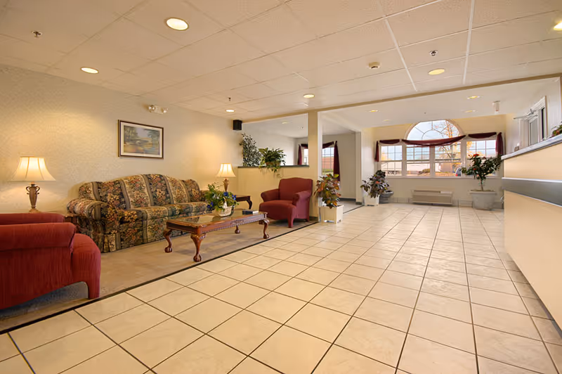 Lobby seating area with a patterned sofa, red armchairs, a wooden coffee table, potted plants and large arched windows.