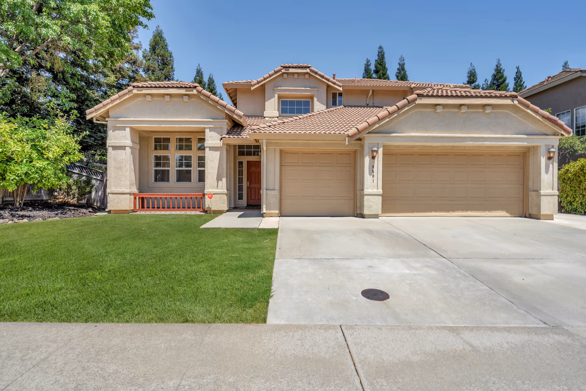 Two-story suburban stucco house with a three-car garage, driveway and green front lawn.