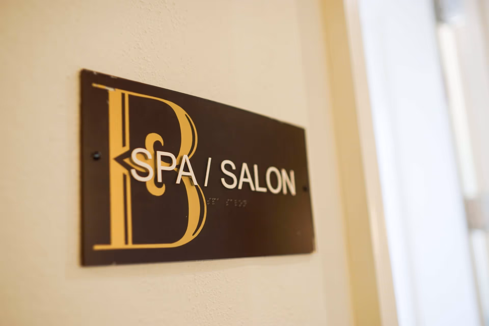 A close-up view of a wall-mounted sign that reads 'SPA / SALON' with a large decorative letter B on the left side, indicating the location of a spa and salon area inside a facility.