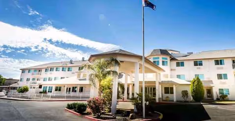 Exterior view of a light-colored senior living facility with a covered entrance and landscaping.