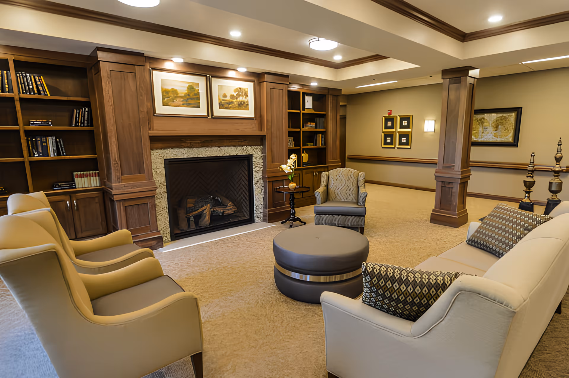 Comfortable lounge with armchairs, a sofa, central ottoman, fireplace, and built-in bookshelves.