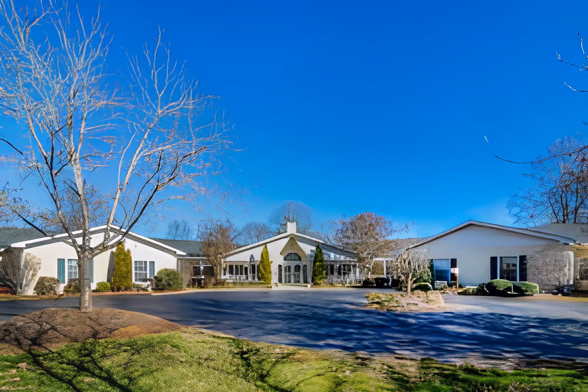 Front view of a one-story senior living facility with a circular driveway, bare trees, and a bright blue sky.