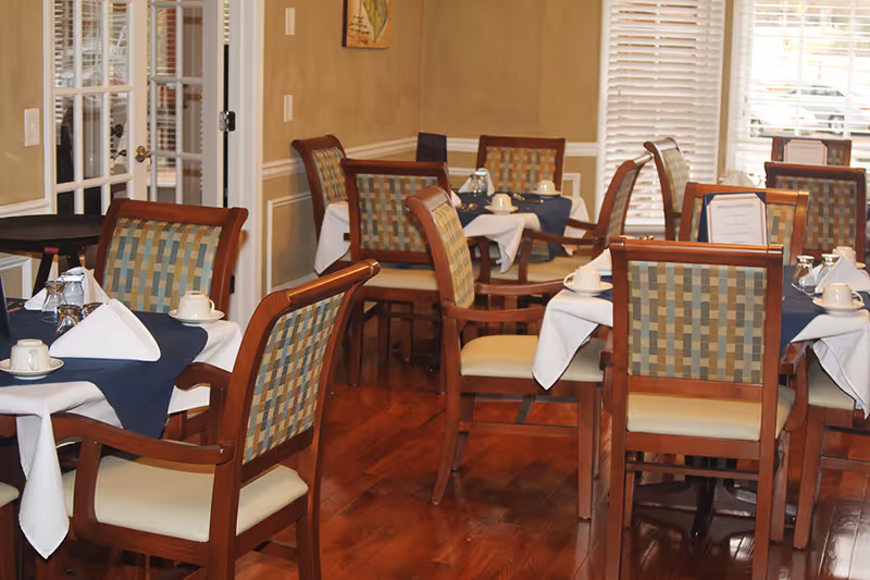 Dining room with wooden tables and upholstered chairs set with napkins, cups, and place settings.