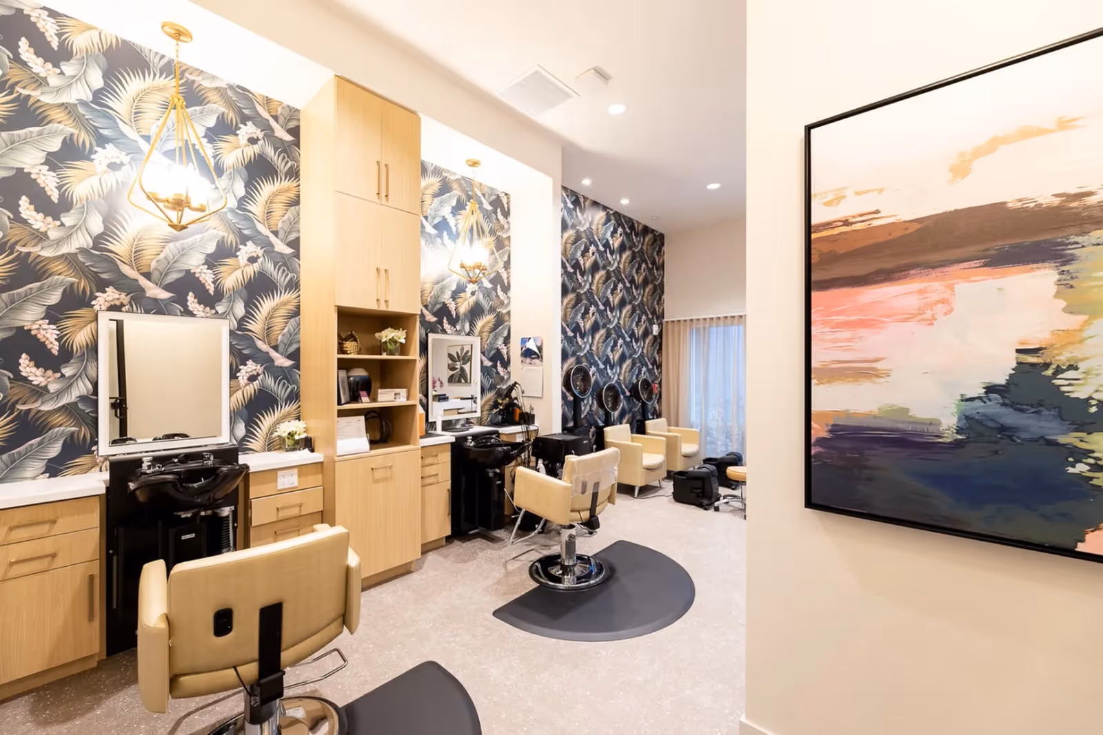 Well-lit salon space with styling chairs, mirrors, washbasins and tropical leaf wallpaper.