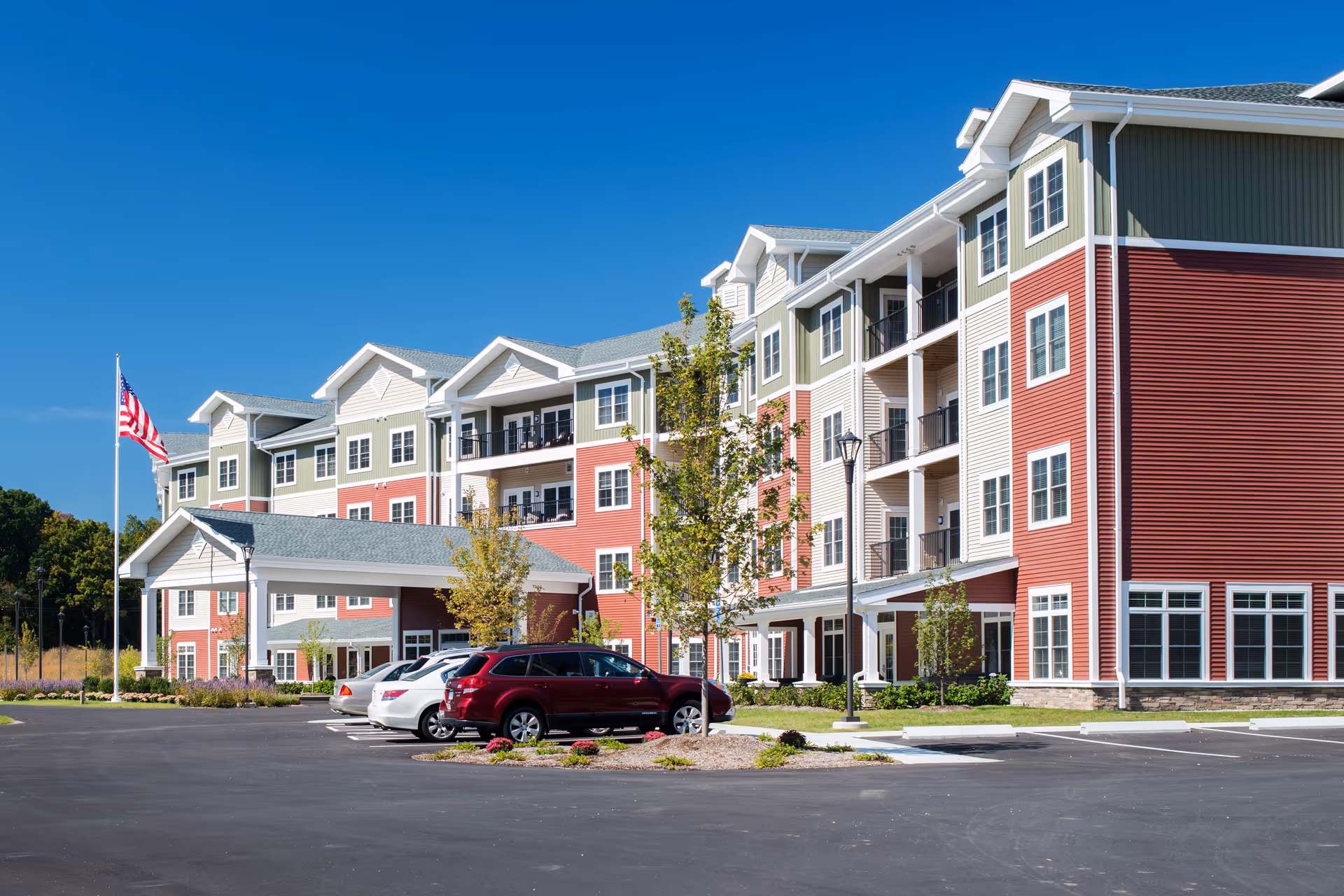 Colorful multi-story senior living building with parking lot and American flag.