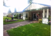 Exterior view of Americana Health & Rehab Center showing the entrance with a covered walkway, green lawn, and a sign near the sidewalk.