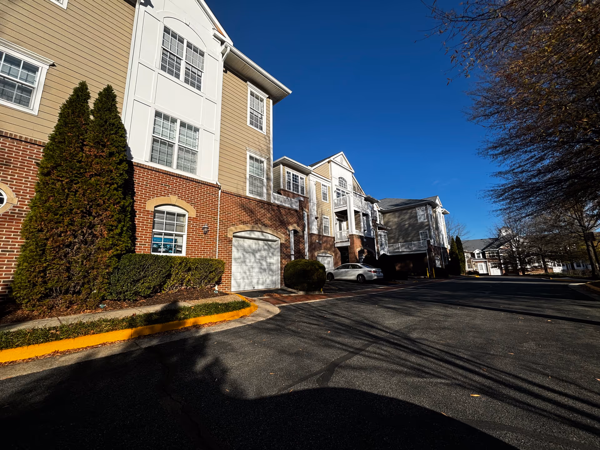 Multi-story brick-and-siding senior residence with garages, balconies, and parked cars along a sunny street.