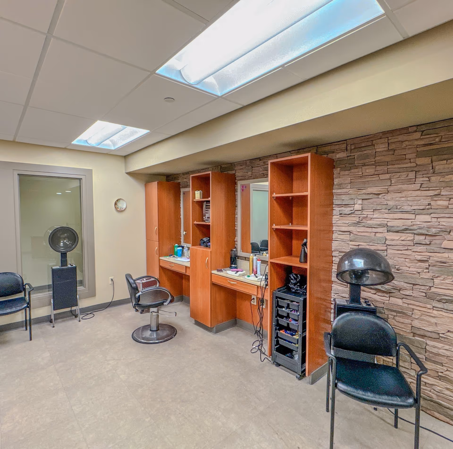 Small salon room with styling chairs, hooded dryers, mirrors and wooden shelving against a stone accent wall.