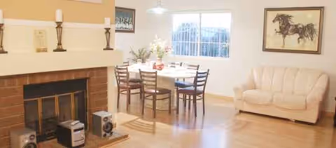Senior care facility living room with a fireplace, dining table, and beige sofa.