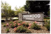 Stone entrance sign reading 'CREEKWOOD APARTMENTS' surrounded by landscaped flowers and trees.