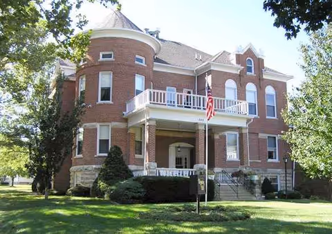 Front view of a red brick senior living building with a balcony and flagpole.