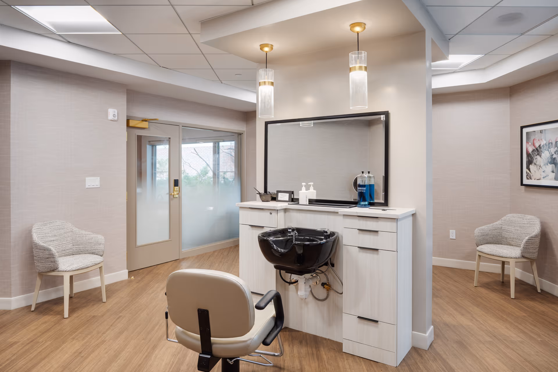 Modern salon hair-washing station with a styling chair, black sink, mirror and seating in a communal interior space.