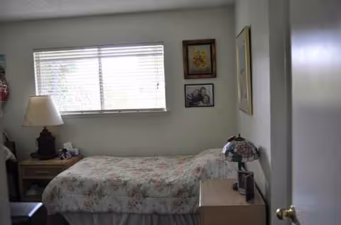 A small bedroom with floral bedspread, nightstands, lamp, and window.