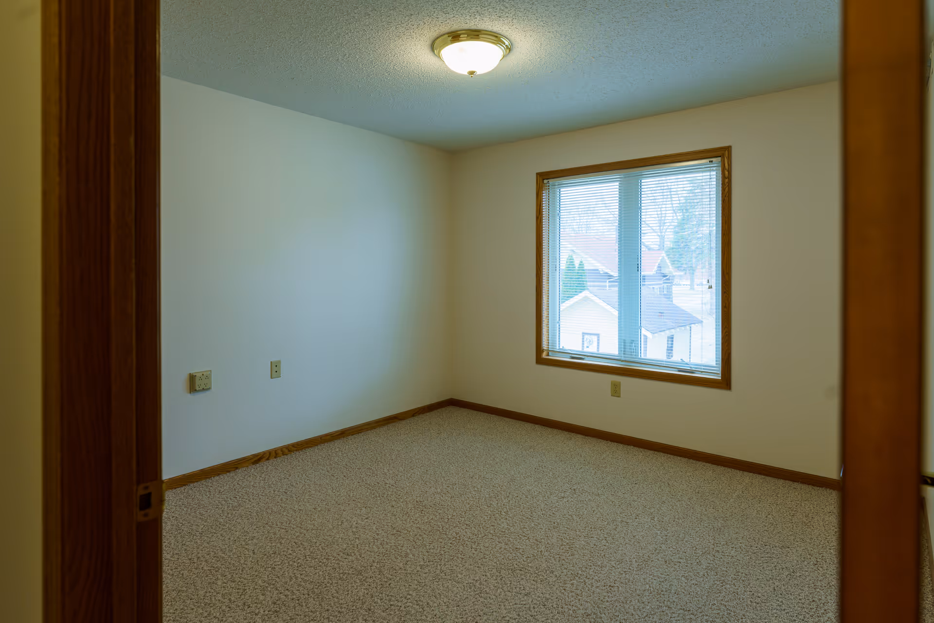 Empty bedroom with beige carpet, a window with wood trim, and a ceiling light fixture.