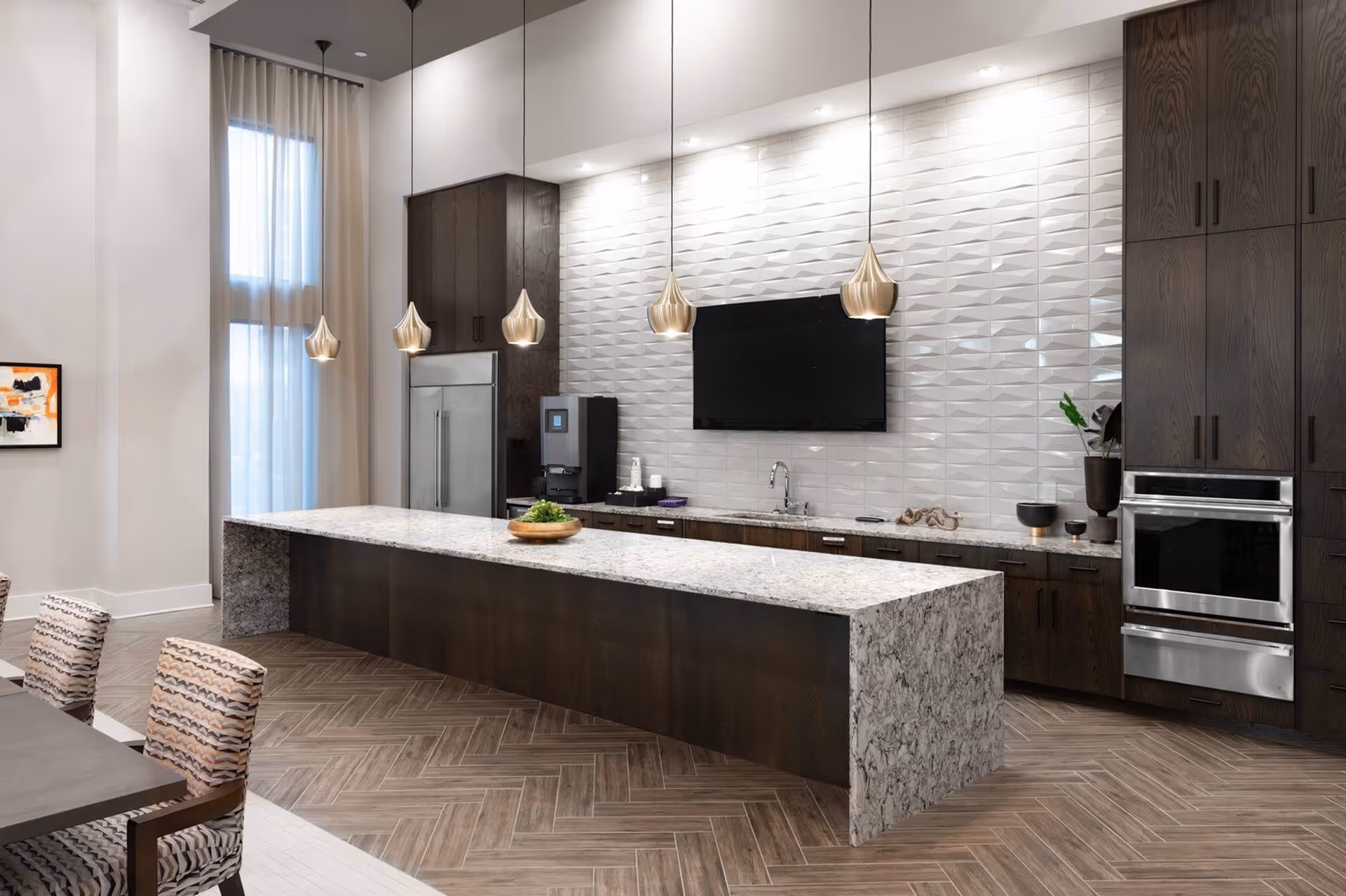 Modern communal kitchen with a long marble island, pendant lights, stainless appliances and seating.