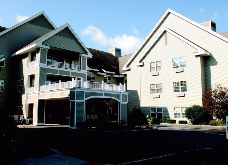 Front exterior of a multi-story senior living building with a covered entrance, balconies, and a driveway.