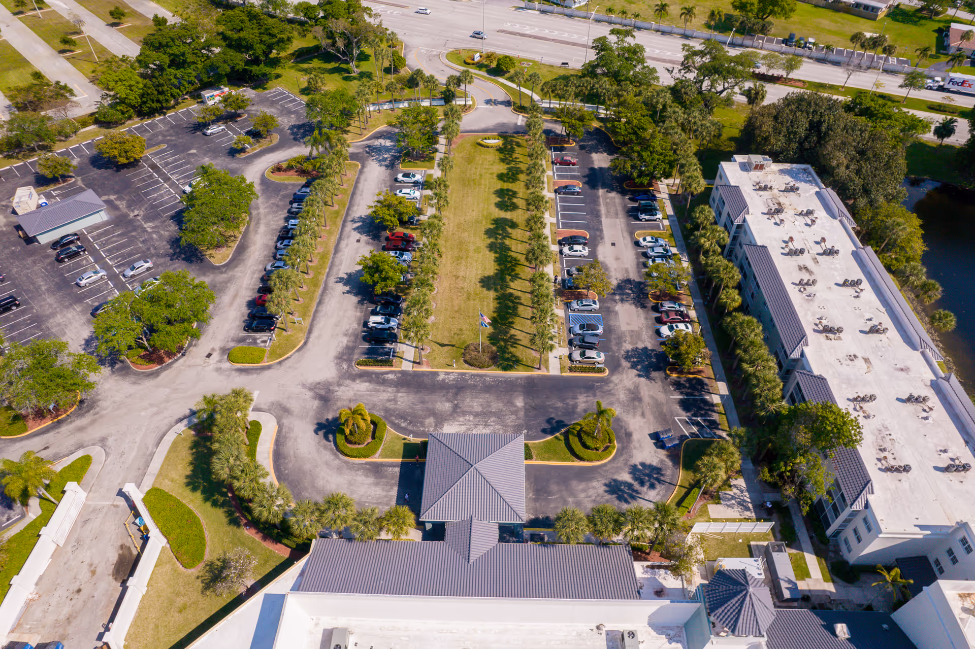 Aerial view of Oasis Living Quarters showing parking lots, a landscaped central lawn, driveways, and adjacent buildings.