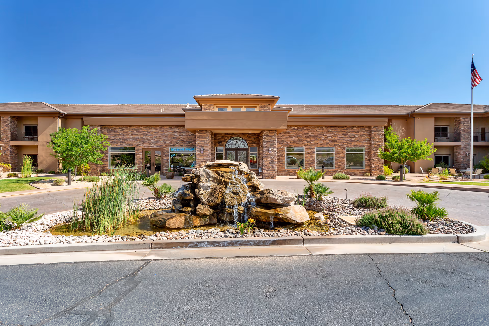 Front exterior of The Retreat at Sunriver with a decorative rock fountain, landscaping, and blue sky.