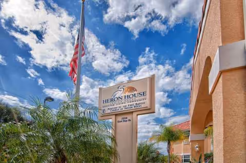 Exterior view of Heron House Assisted Living sign and entrance against blue sky