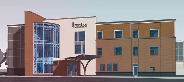 Exterior view of a modern three-story building with a combination of brick and white walls, large glass windows, and a covered entrance. The building has a sign that reads 'Interlude Restorative Suites'.