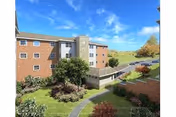 Multi-story brick senior living building with a grassy lawn and curved walkway in the foreground.