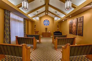 Chapel-like interior with wooden pews facing a small stage and circular window.