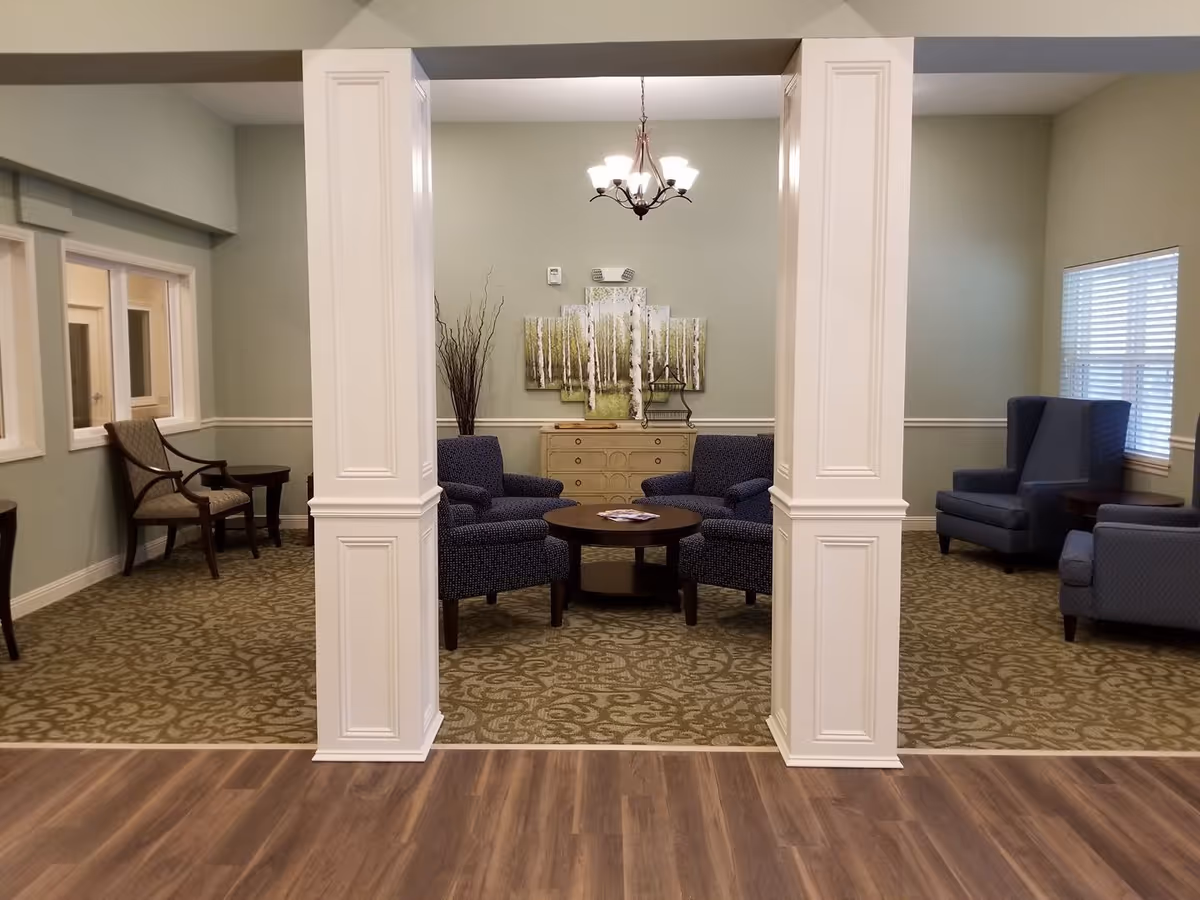 Seating area in a senior living lounge with upholstered chairs, a coffee table, decorative columns, and wall art.