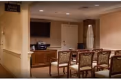 Interior room with rows of chairs facing a media center that includes a television and audio equipment, with beige walls and carpeted floor.