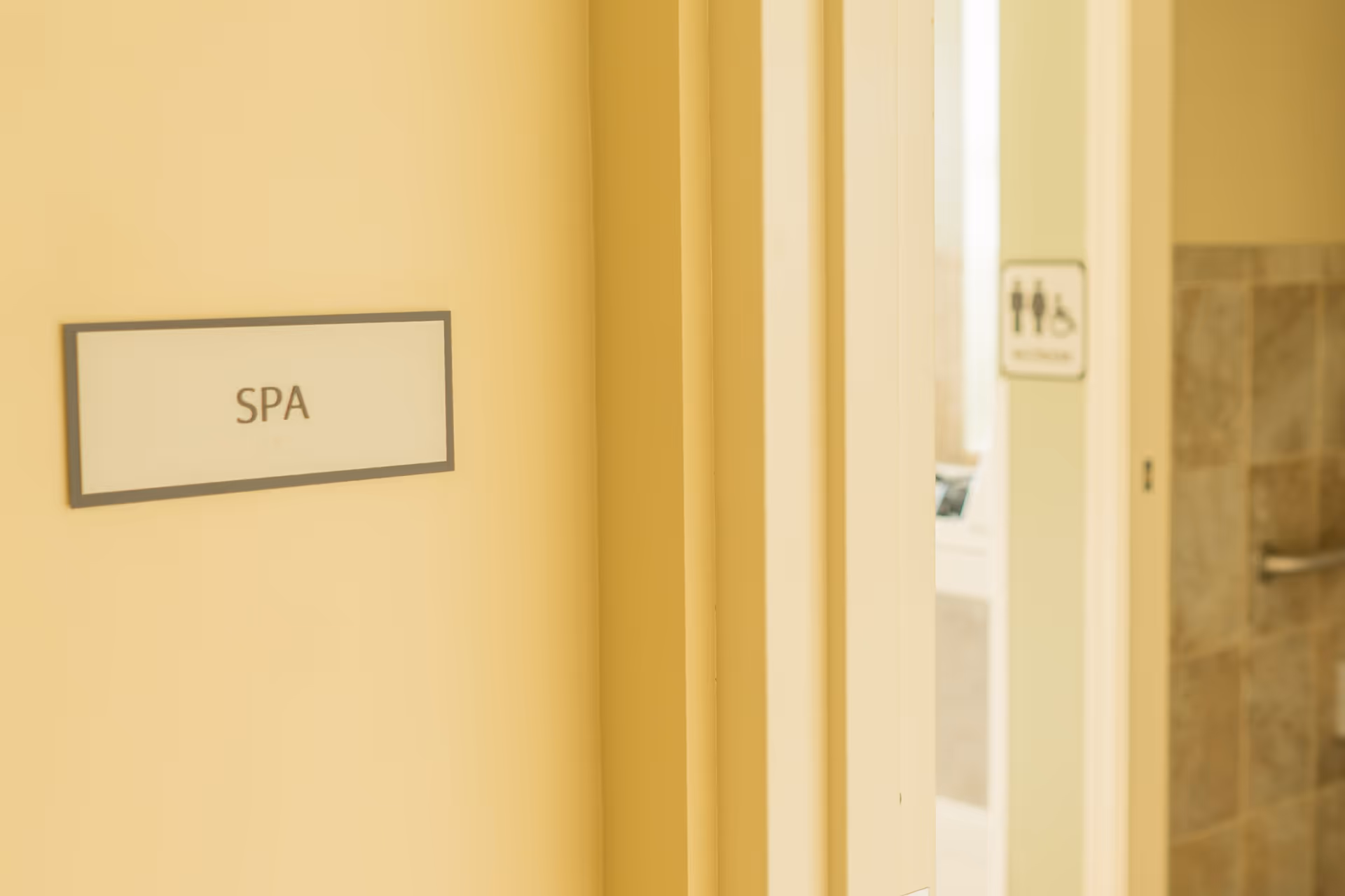 Close-up of a beige wall with a sign that reads 'SPA' next to a partially open door showing a restroom sign and tiled wall inside.