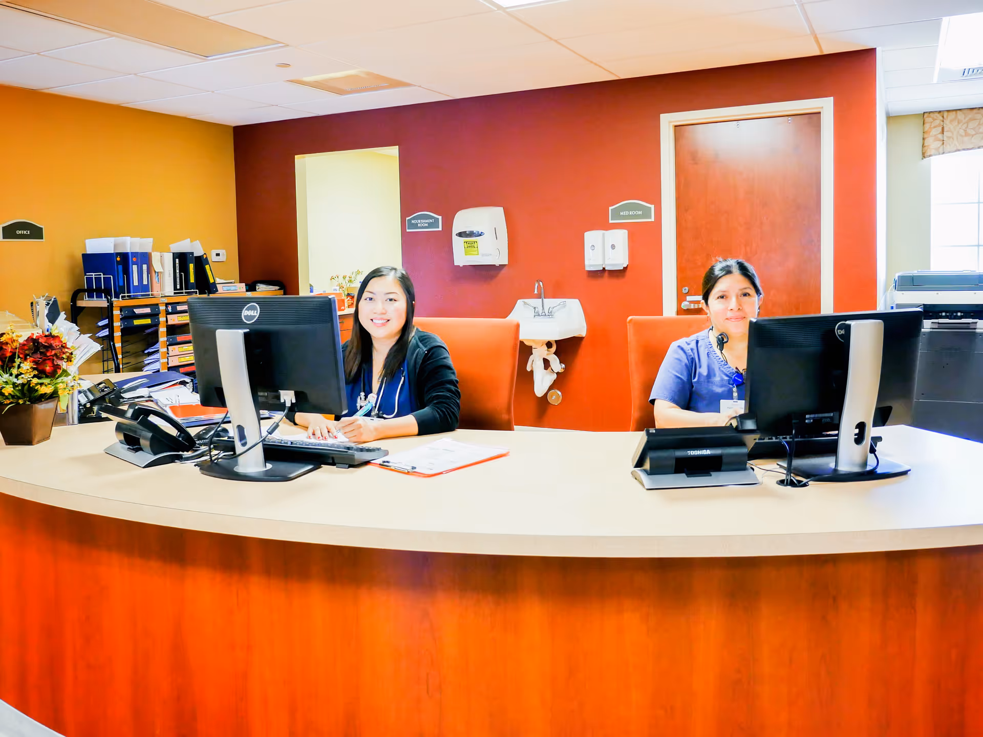 Two staff members working at a reception desk in a senior living facility.