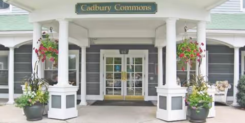 Facade of Cadbury Commons entrance with columns, plants, and glass doors.