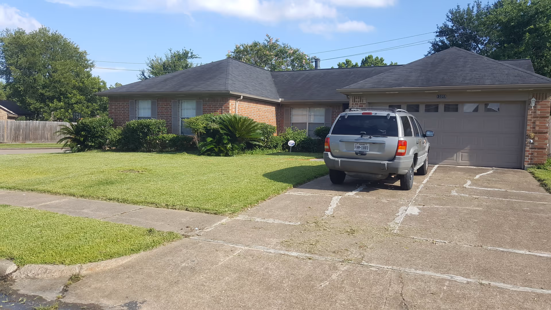 Front view of a single-story brick house with a two-car garage, driveway with a parked SUV, and a neatly mowed lawn.
