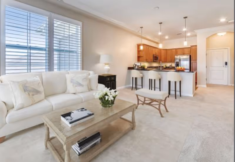Open living room with a white sofa and coffee table facing a kitchen island with three bar stools.