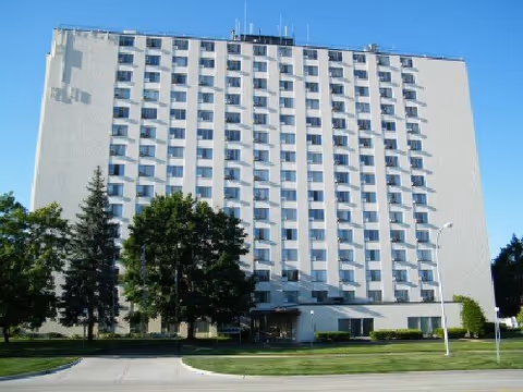Tall multi-story senior living facility exterior with entrance and trees