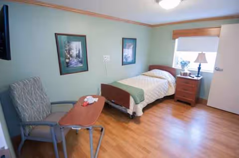 Bedroom in a senior living facility with a bed, chair, nightstand, and window.