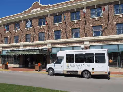 A brick senior living facility facade with a Kennybrook Village bus parked in front.