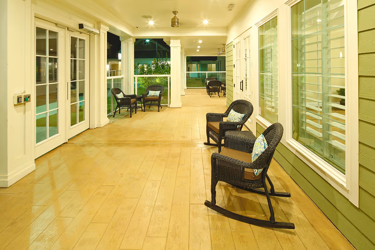 Covered porch with wicker rocking chairs and seating along a building's windows.