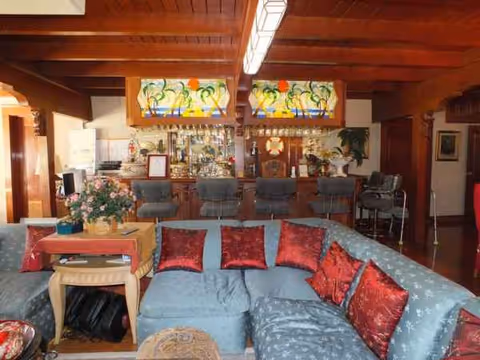 Cozy lounge with blue sectional, red cushions, flowers, and a bar area in the back.