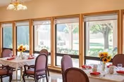 Bright dining room with tables set for meals, sunflowers in vases, and large windows.