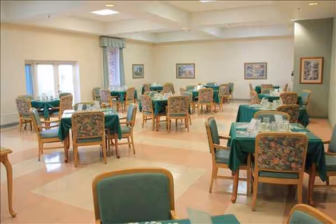 A spacious dining room with round tables covered in green tablecloths and chairs.
