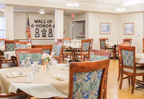 Dining room with multiple tables set for a meal and a 'Wall of Honor' display on the far wall.