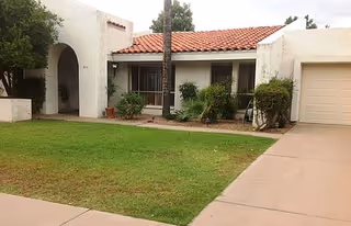 Front exterior of a single-story stucco house with a tiled roof, lawn, driveway, and attached garage.