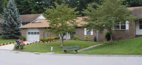 Front exterior view of Creekside Village Retirement Residence with brick facade, lawn, and bench.