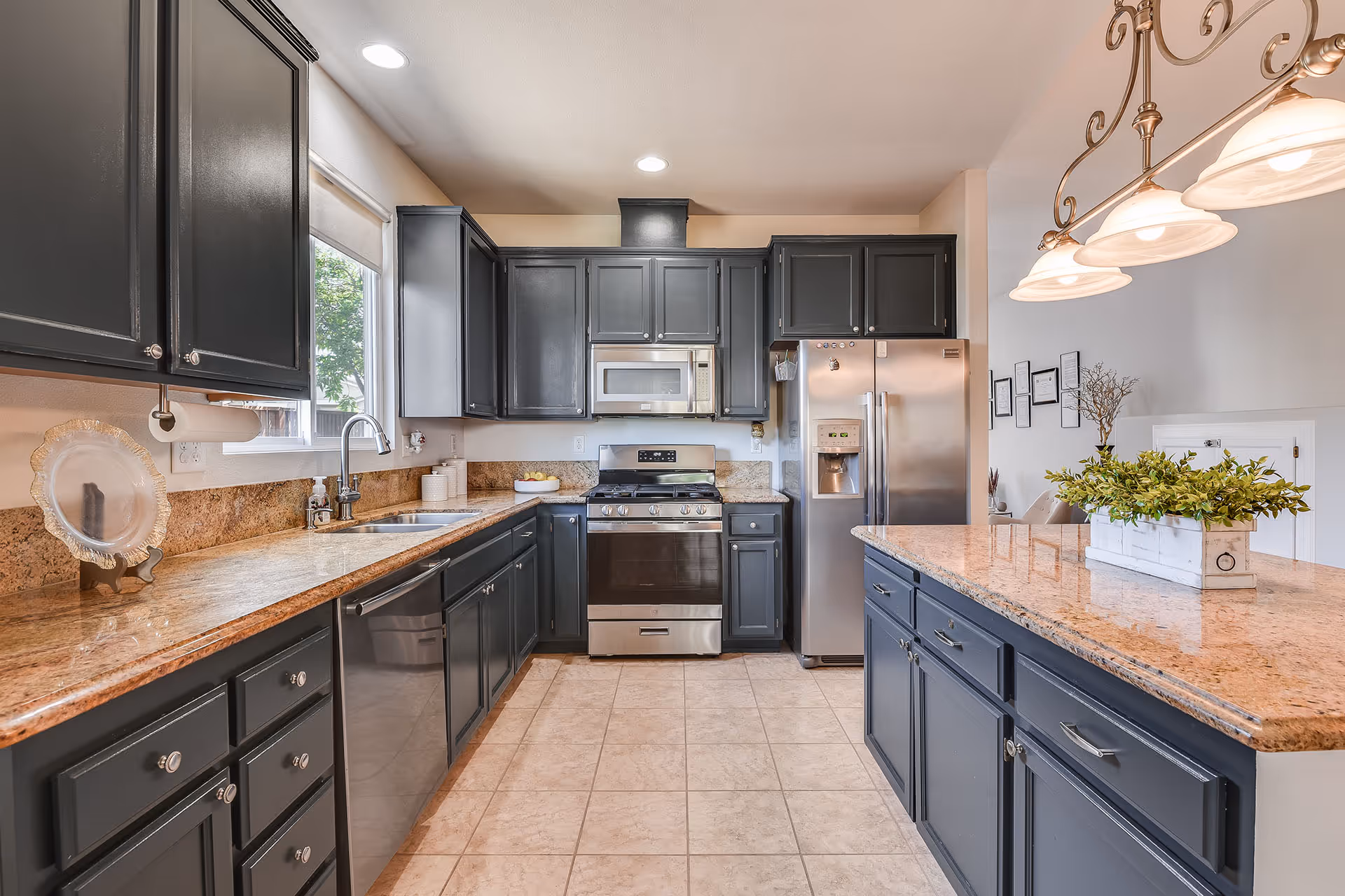 Modern kitchen with dark cabinets, granite countertops, stainless steel appliances, and an island under pendant lights.