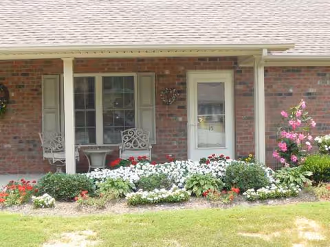 Brick building exterior with front porch, white doors, and colorful flower garden.