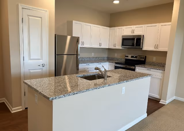 Modern kitchen with white cabinets, granite countertops, stainless steel refrigerator, stove, microwave, and a sink on the kitchen island.